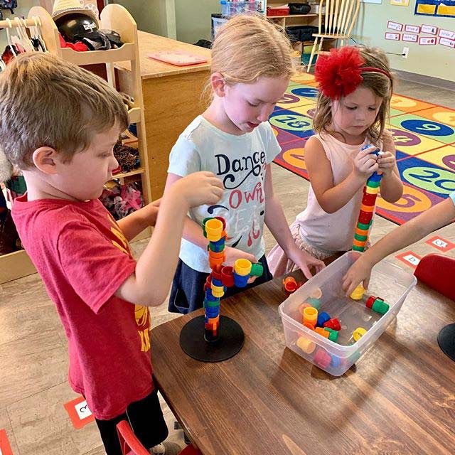 Three preschool kids building blocks together focusing on the table block towers
