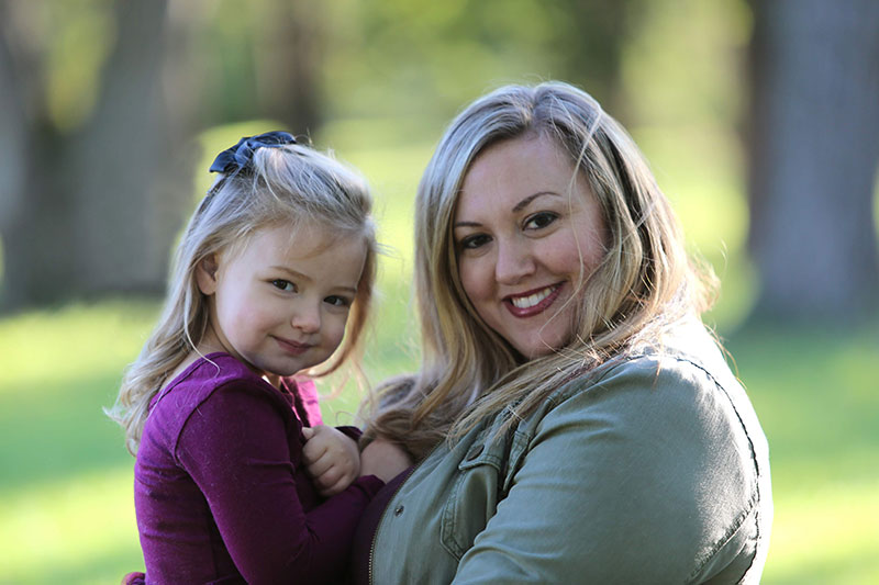 Michelle holding a girl outside in her arms, both looking at camera and smiling